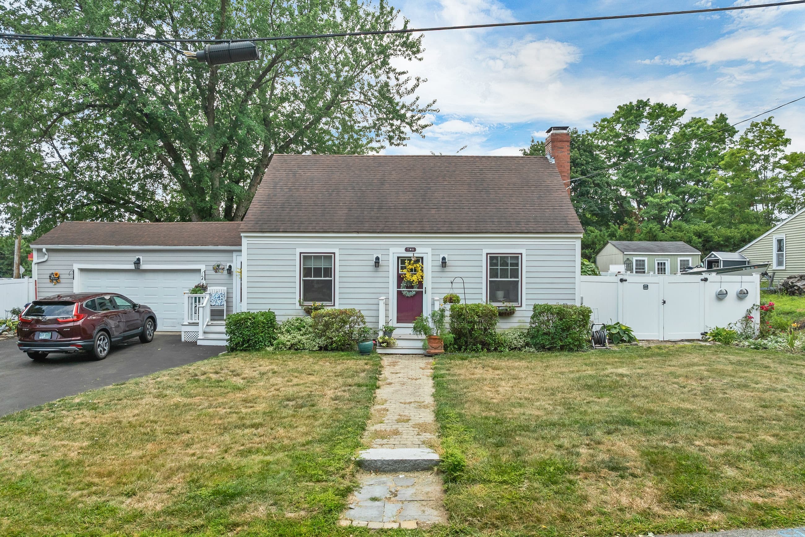 Front elevation of the grey clapboard Cape, with a red front door, a granite walkway, and the attached garage at left