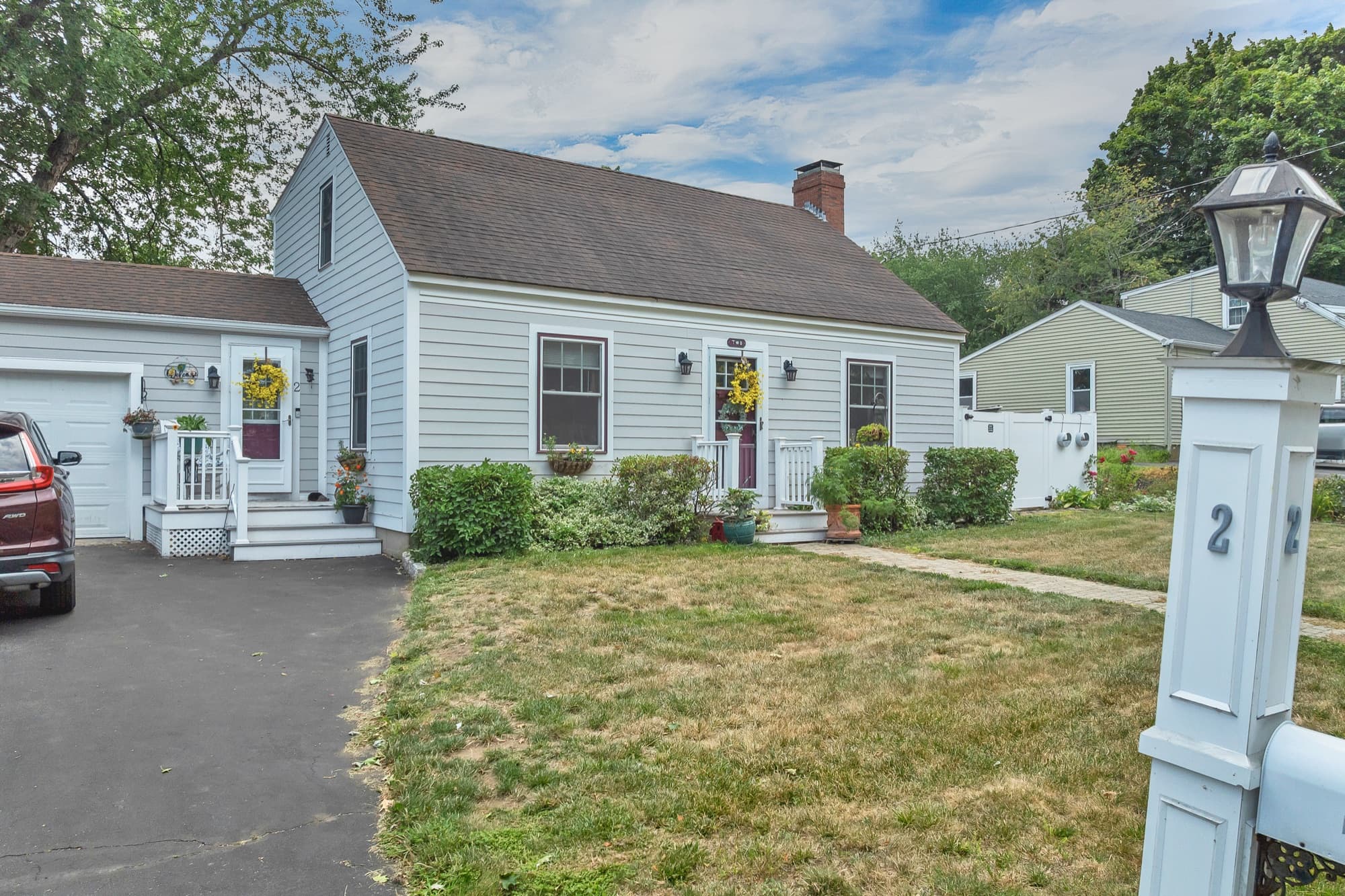 The house from the driveway, showing the steep gabled roof, brick chimney, and the garage ell