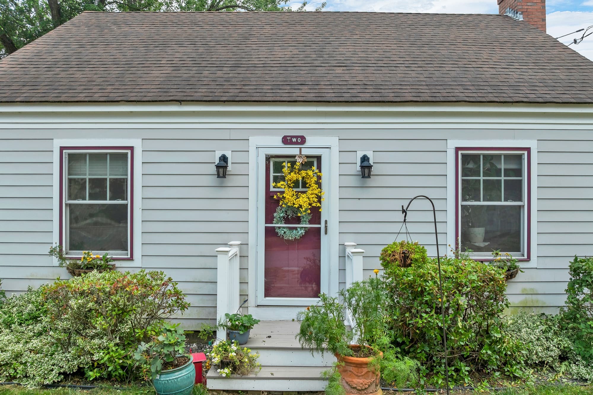 Front entry with a red door, a sunflower wreath, and planting beds along the foundation