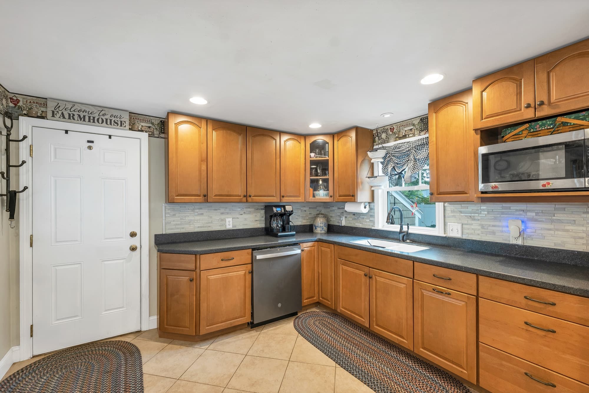 Kitchen with raised-panel wood cabinets, dark counters, a tile floor, and a stainless dishwasher