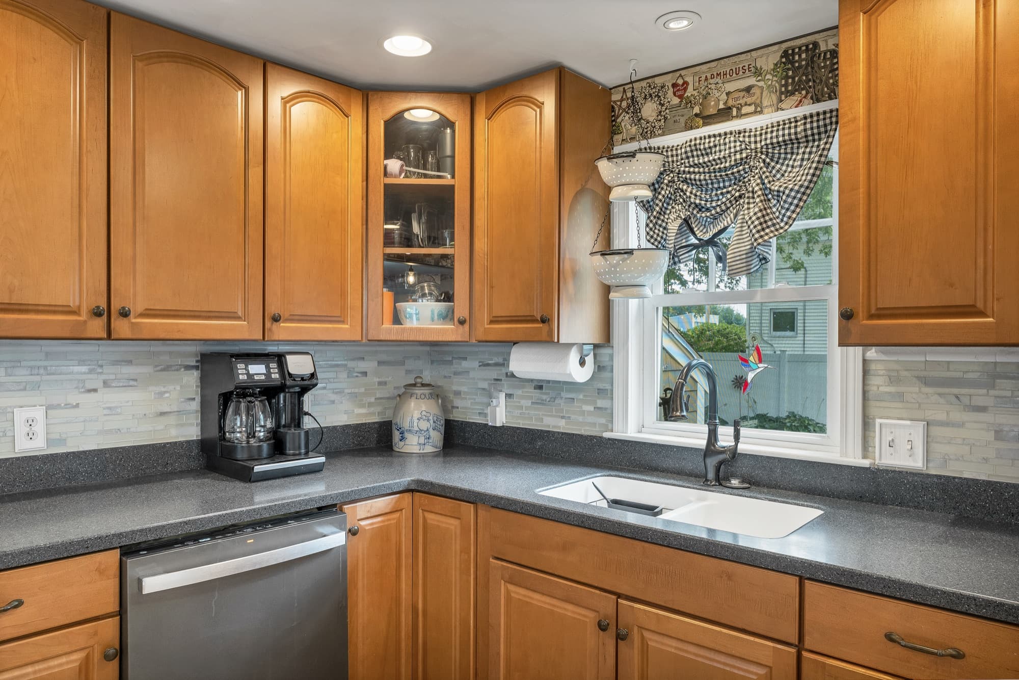 Kitchen sink under a window, with a tiled backsplash and glass-front upper cabinets
