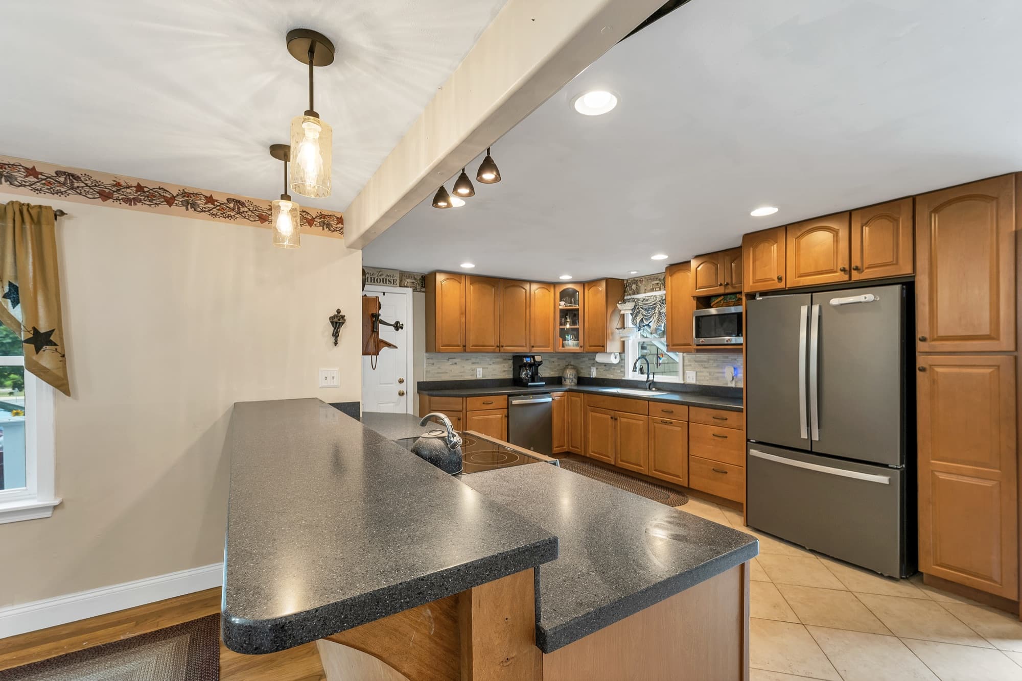 Kitchen island with a raised bar counter, looking toward the stainless refrigerator and wall oven