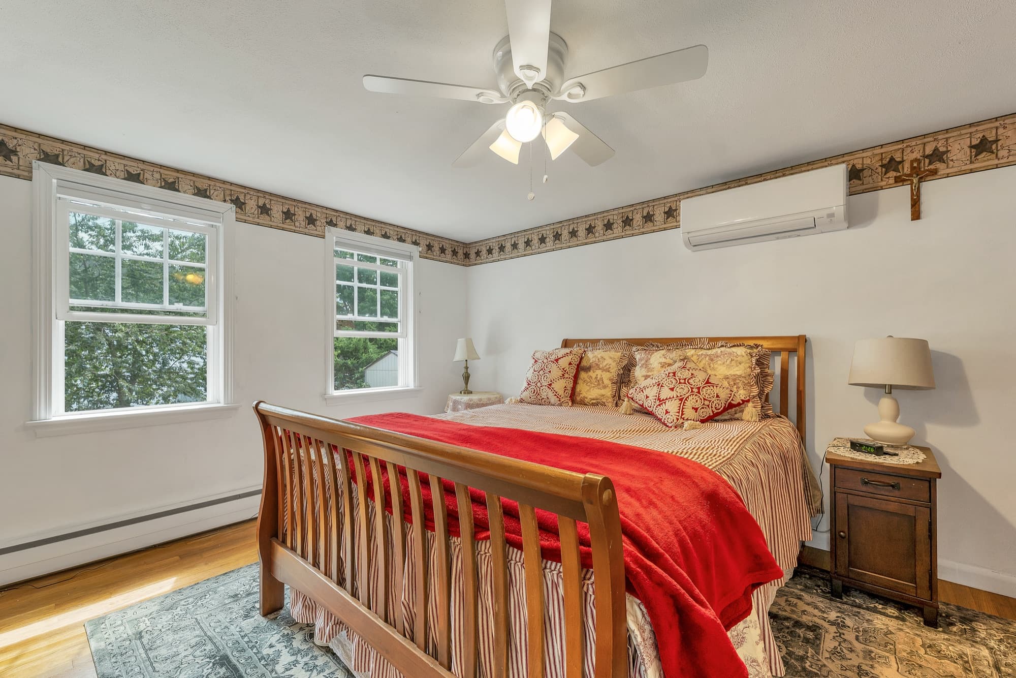 Primary bedroom with hardwood floors, a ceiling fan, and a wall-mounted mini split