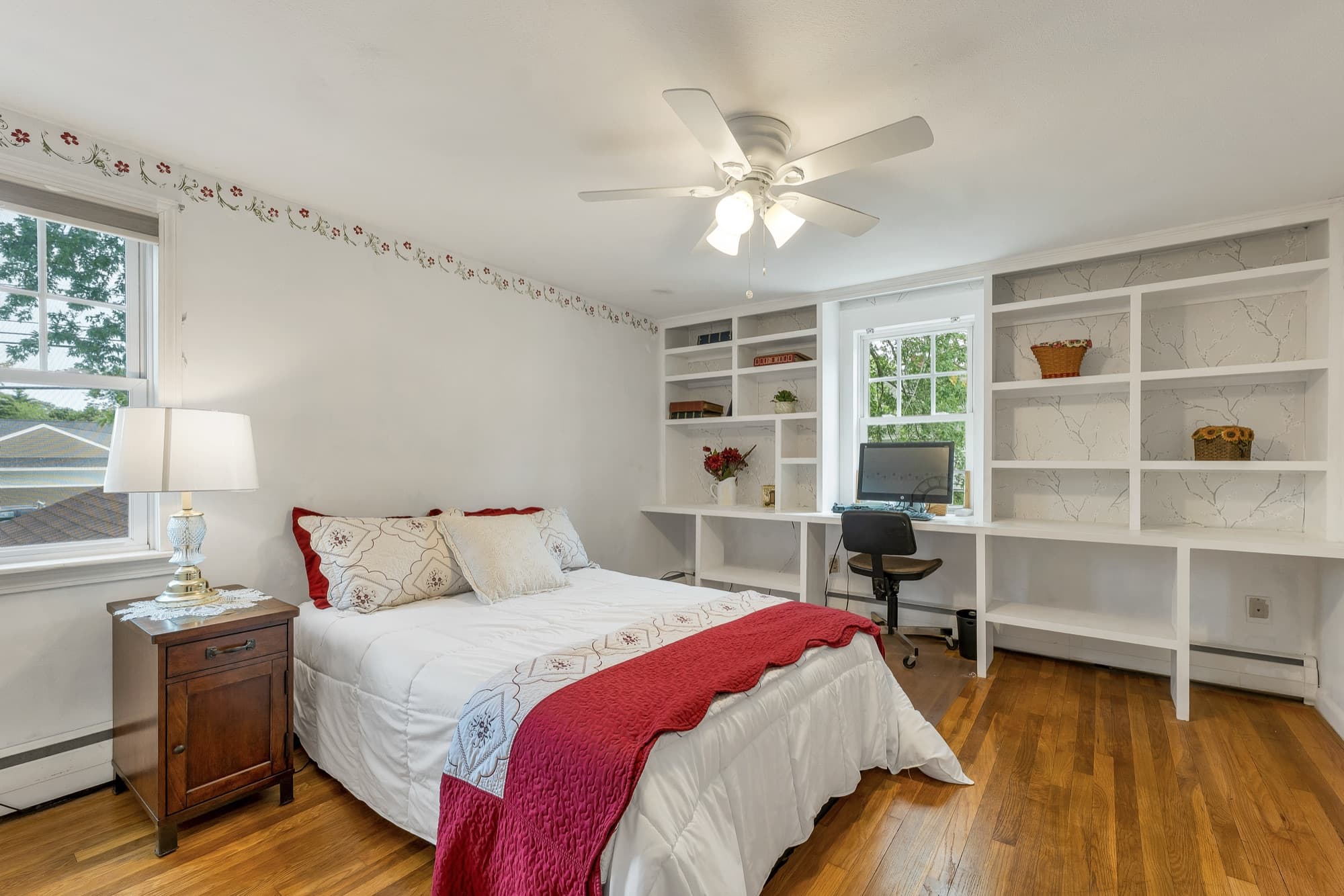 Second bedroom with built-in white shelving, hardwood floors, and a ceiling fan