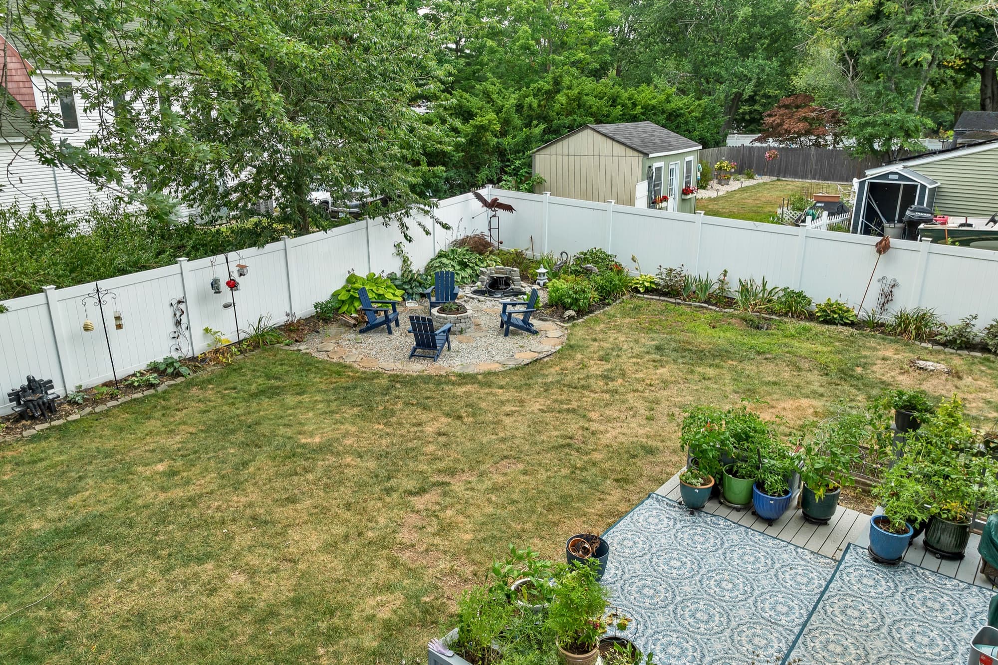 Fenced backyard with a paver patio, a fire pit, garden beds, and potted plants